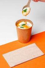 Charger l'image dans la galerie, Cuillère réutilisable en canne à sucre soulevant une soupe crémeuse d'un gobelet en kraft sur fond orange.
