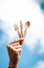 Charger l'image dans la galerie, Hand holding biodegradable fork, knife, and spoon against a blue sky backdrop.