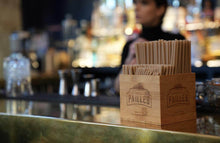 Charger l'image dans la galerie, Eco-friendly sugarcane straws displayed in a wooden holder at a bar, highlighting sustainable beverage options.