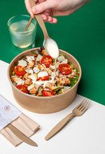 Charger l'image dans la galerie, hand drizzling dressing on a salad with wooden cutlery in a biodegradable bowl on a colorful background.