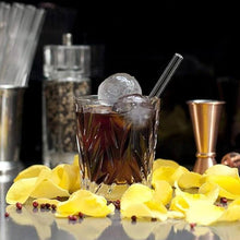 Charger l'image dans la galerie, Verre de cocktail avec paille en verre borosilicate, glace et pétales de fleurs, décor raffiné pour une expérience élégante.