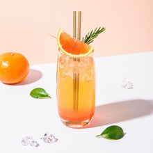 Charger l'image dans la galerie, Cocktail in a glass with bagasse straws, garnished with orange and rosemary, surrounded by ice and fruit.