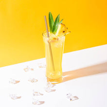 Charger l'image dans la galerie, Refreshing cocktail with a bagasse straw, garnished with pineapple and mint, on a bright yellow background.