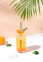 Charger l'image dans la galerie, Cocktail glass with a gold straw, orange slice, and palm leaf in a bright setting, showcasing eco-friendly drinking.